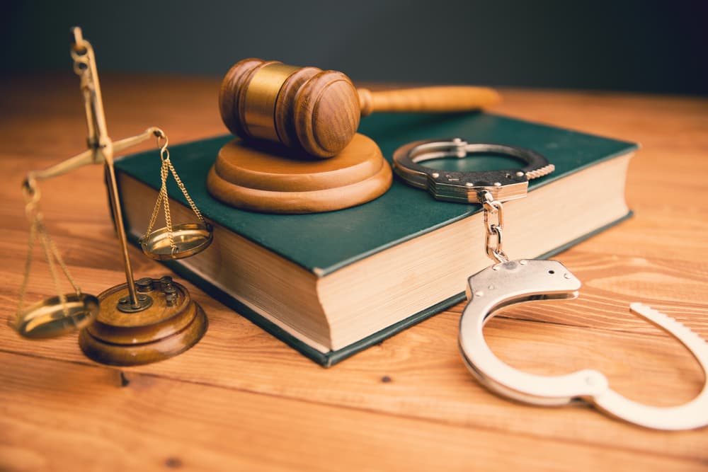 Scales of justice, a gavel, and handcuffs arranged on a table.