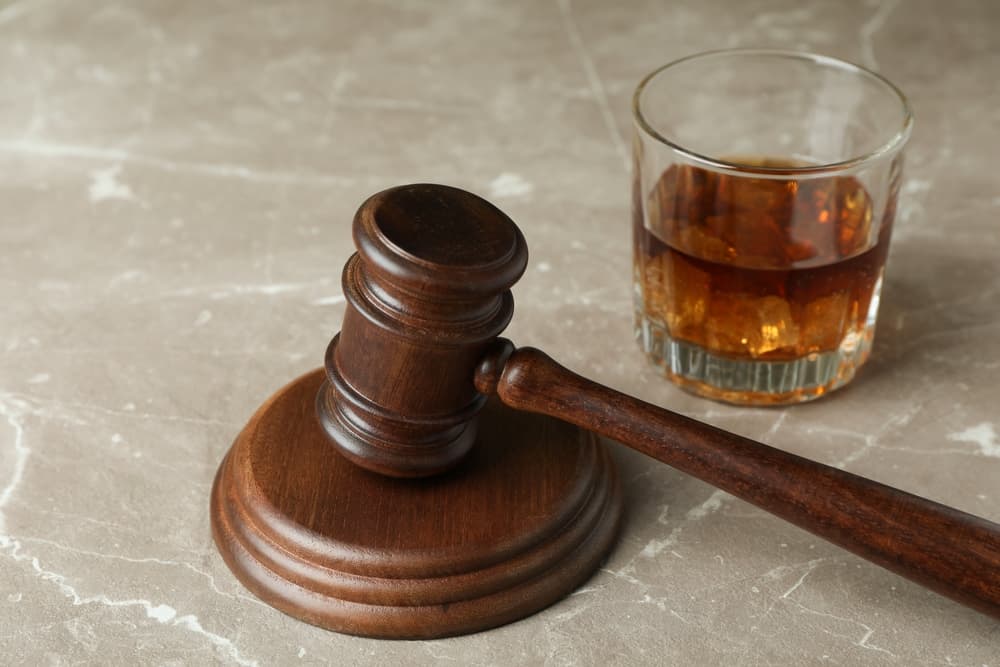 Judge gavel and glass of whiskey on gray textured table